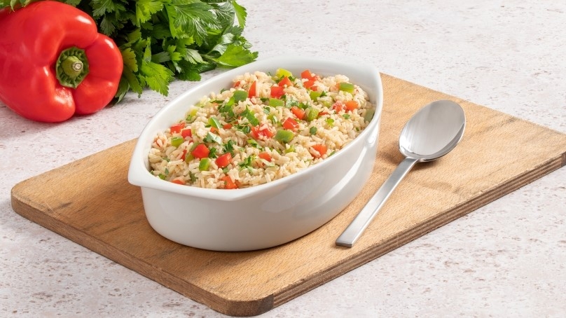 Baked Brown Rice with Peppers in baking dish, wood cutting board, silver spoon, stone coun ter top