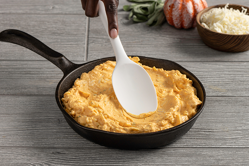 Hand stirring pumpkin and cream cheese mixture in cast iron skillet