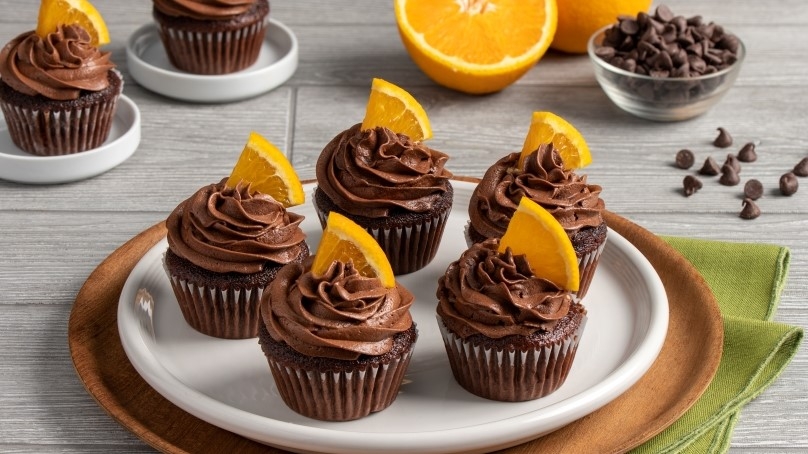 Double Chocolate Orange Cupcakes with orange wedges on white plate, wood plate, green napkin, gray wood