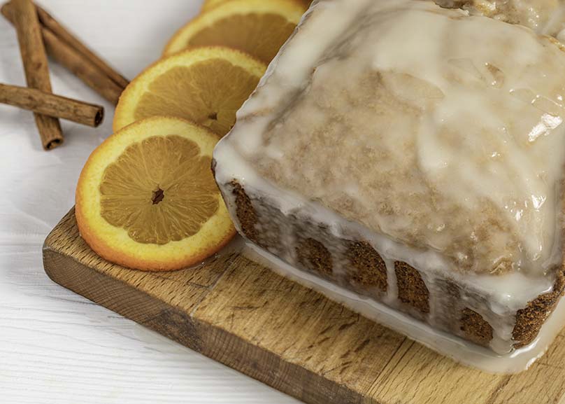 Glazed Eggnog Pound cake on cutting board with orange slices and cinnamon stocks