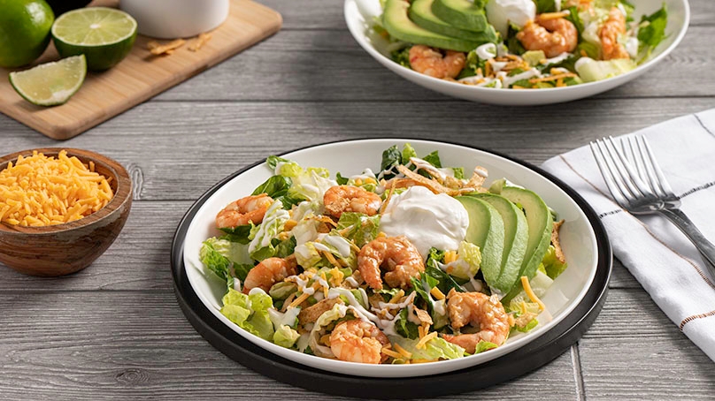 Garlic Lime Shrimp Taco Salad on plates, wood table, limes, cheese, napkin and silverware