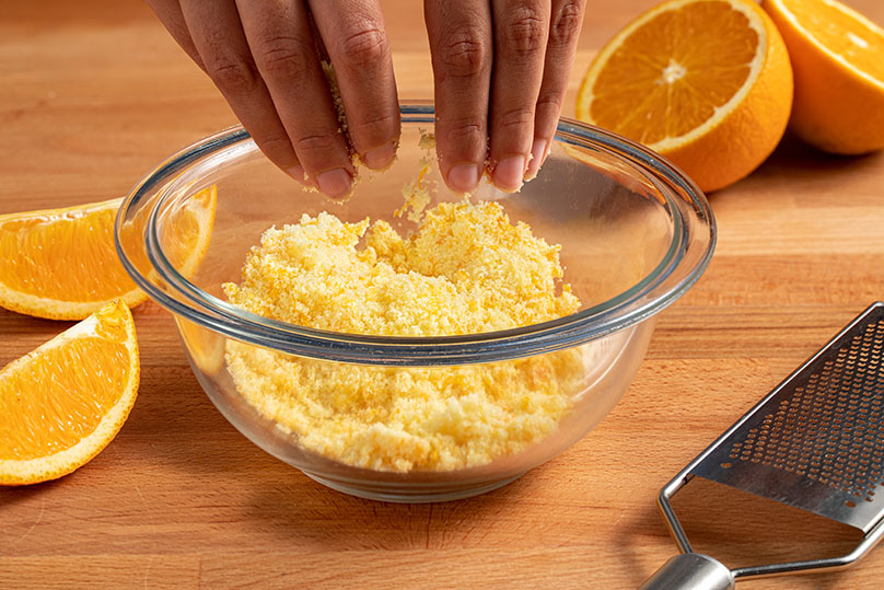 Sugar and orange zest being rubbed together the in a small bowl using your fingers