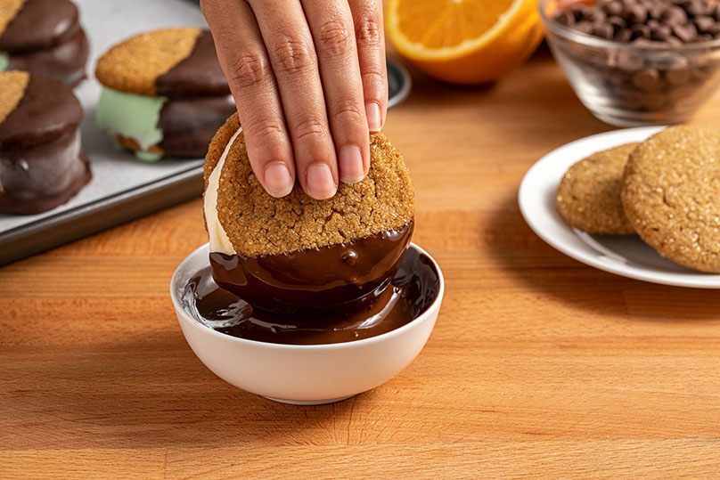 Hand dipping ice cream sandwiches onto the melted chocolate 