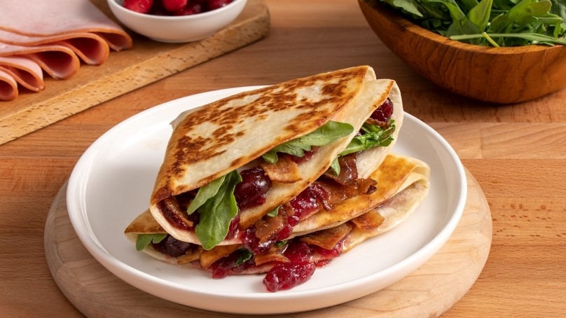 Leftover Cranberry and Bacon Grilled Cheese Tortilla Wrap on white plate,, wood table, miscellaneous ingredients