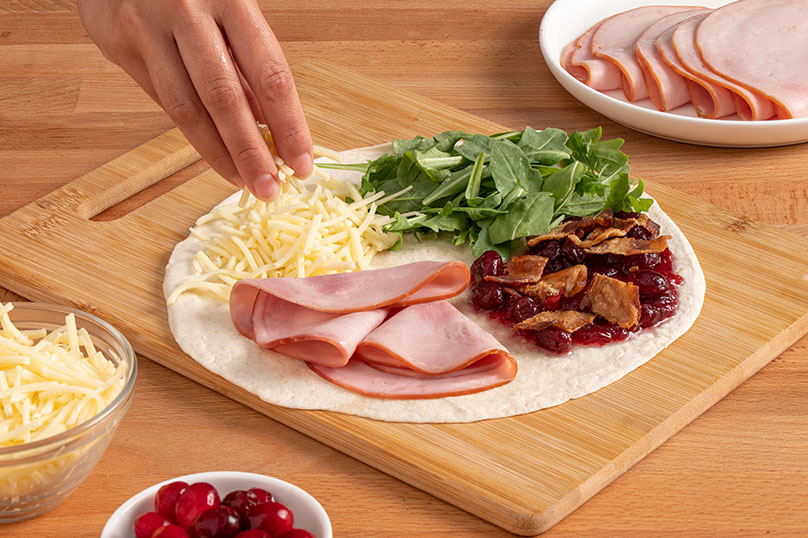 toritlla and ingredients divided into quadrants, arugula, cranberry sauce with bacon, sliced ham, hand sprinkling cheese