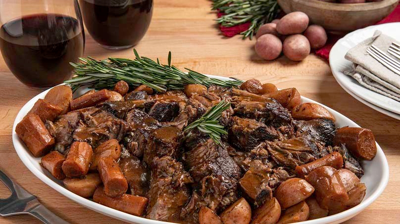 Red Wine Pot Roast, carrots, rosemary, red skin potatoes, serving fork, red wine glasses,  napkins, plates, wood bowl, wood table