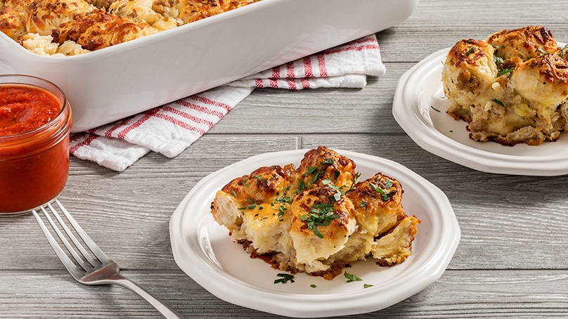 Sausage and Cheese Pull Apart Bread on white plates, fork, jar of marinara sauce for serving, baking dish in background on red and white checkerboard napkin