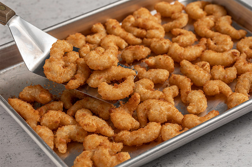 Metal spatula lifting popcorn shrimp out of metal sheet pan of cooked popcorn shrimp