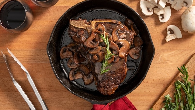 Tender T-Bone Steak with Red Wine Sauce in cast iron skillet, wood counter, miscellaneous fresh ingredients