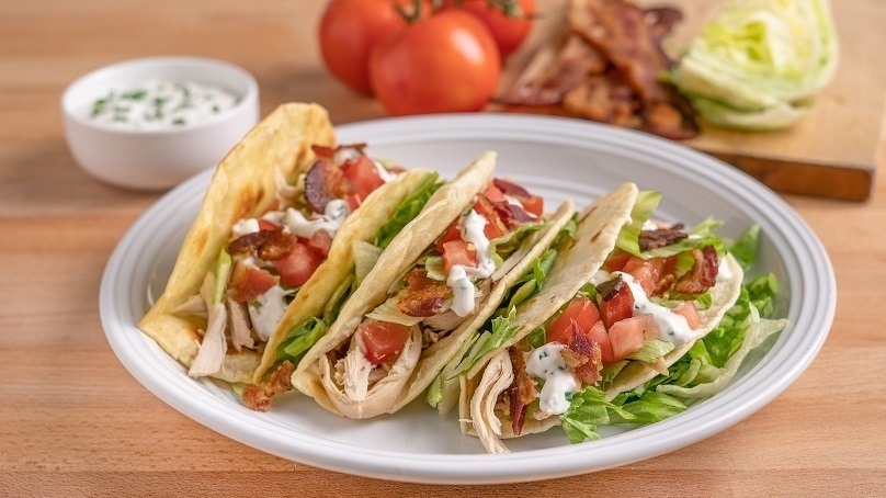 Chicken BLT Tacos on white plate, wood table, sour cream dish, tomatoes, bacon stripe, lettuce