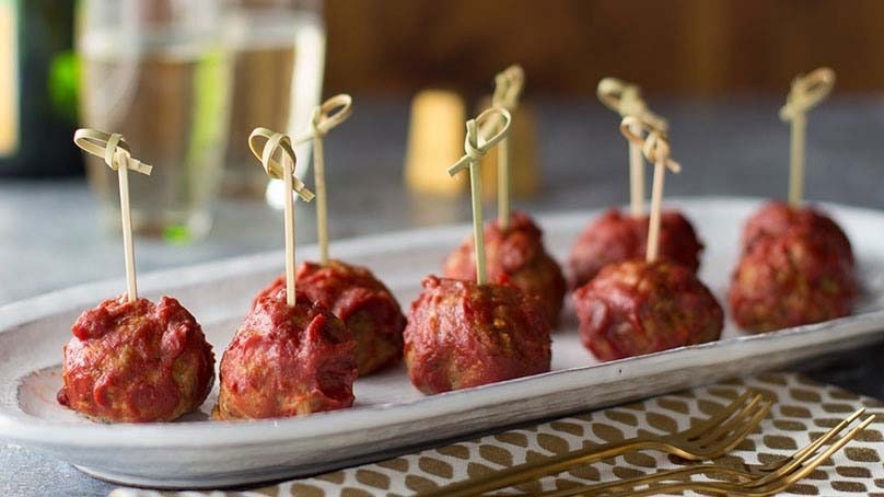 Champagne Turkey Meatballs with toothpicks on serving dish, festive napkin, drinks in background 