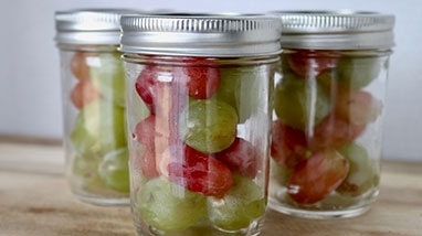 Three mason Jars with Fruit on wood table.