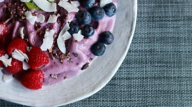 Smoothie bowl with fresh berries and coconut flakes, white antique bowl, blue woven tablecloth