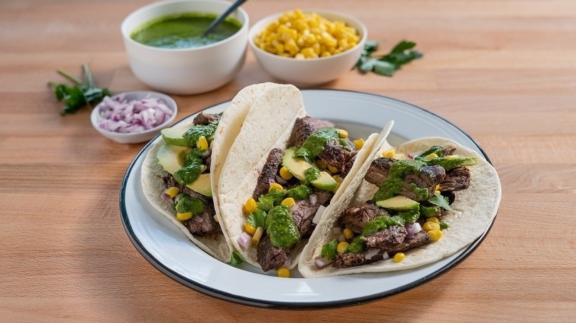 Chimichurri steak tacos on a plate with sauce next to it.