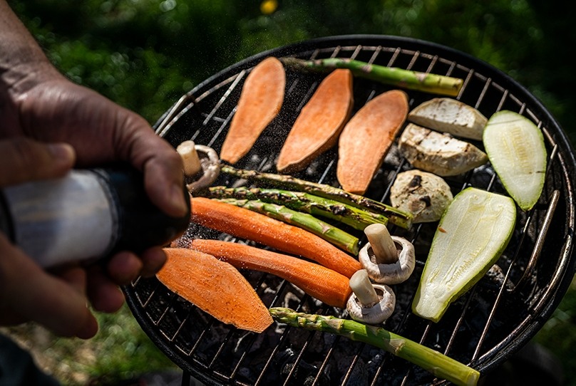 Hand salting carrots, asparagus, mushrooms, sweet potatoes on grill