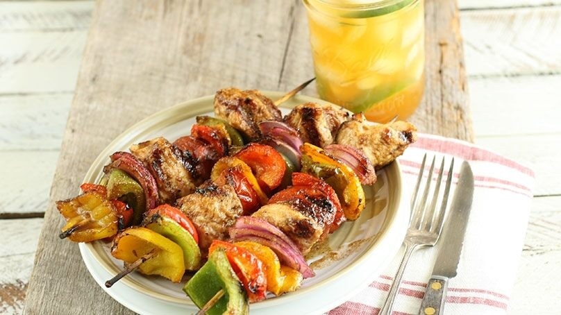 Sweet Maple BBQ Chicken Kebobs on white plate, glass of juice, red striped napkin, fork, knife, wood table