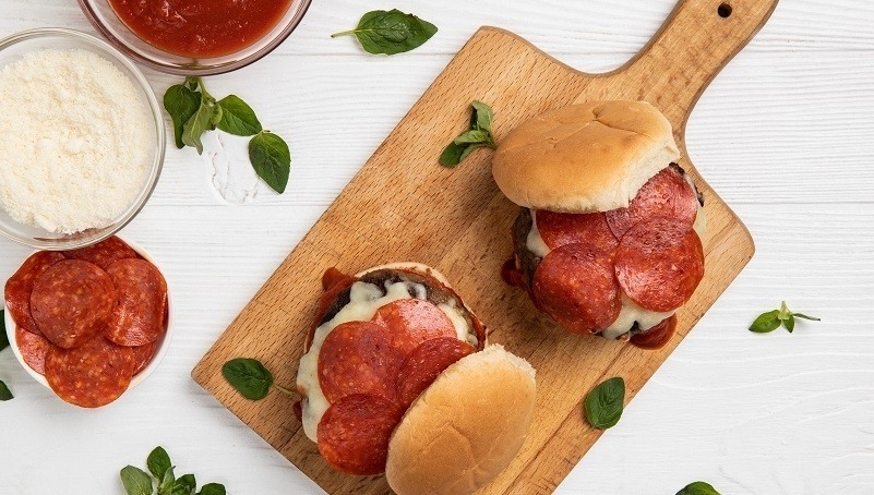Grilled Pizza Burgers on wood paddle, serving bowls of pepperoni, mozzarella cheese, and marinara sauce, fresh basil leaves, white wood table