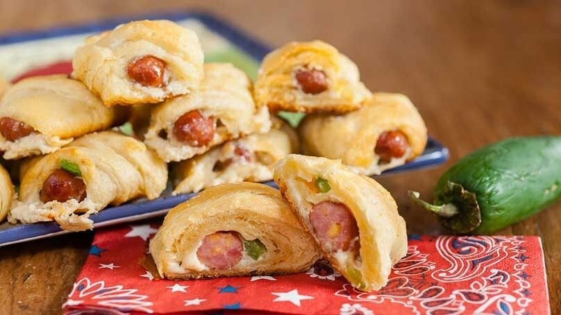 Jalapeno Popper Pigs in a Blanket on blue plate, jalapeno pepper, red white and blue napkin, wood table