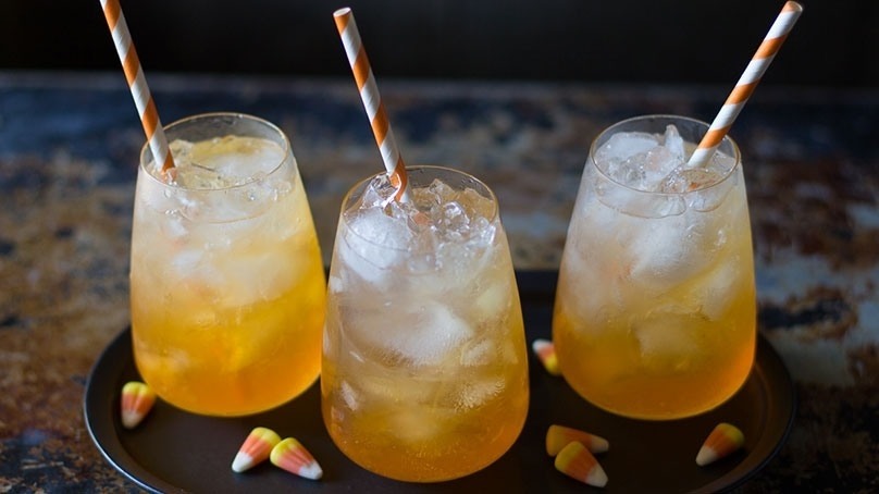 3 cups of Candy Corn Punch with orange striped straws, candy corn on plate