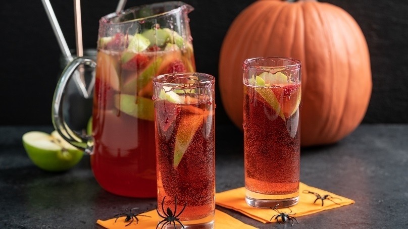 Two glasses of vampire punch on Halloween napkins with a pitcher behind.