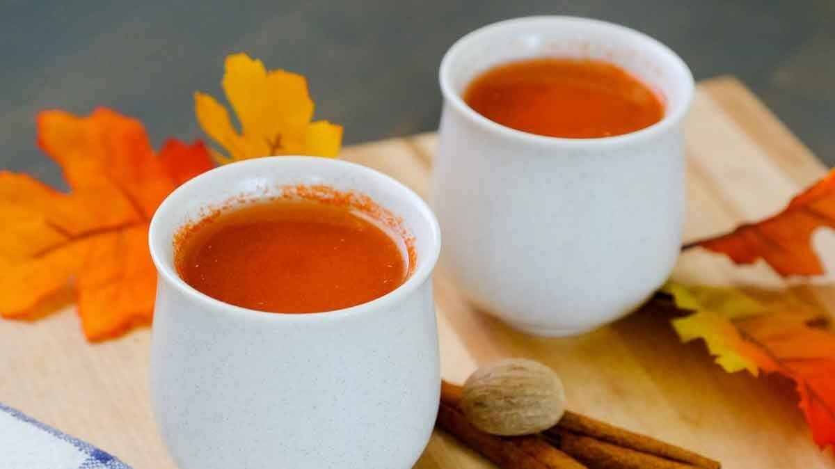 Warm Apple Carrot Drink in white cups on cutting board with fall colored leaves