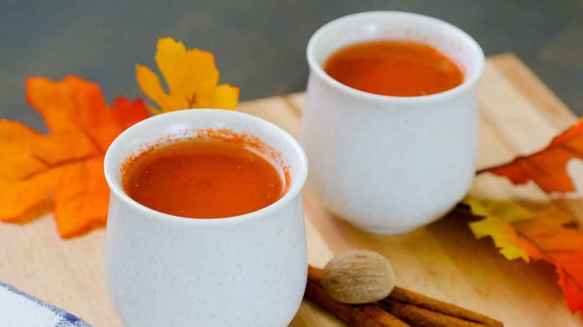 Warm Apple Carrot Drink in white cups on cutting board with fall colored leaves