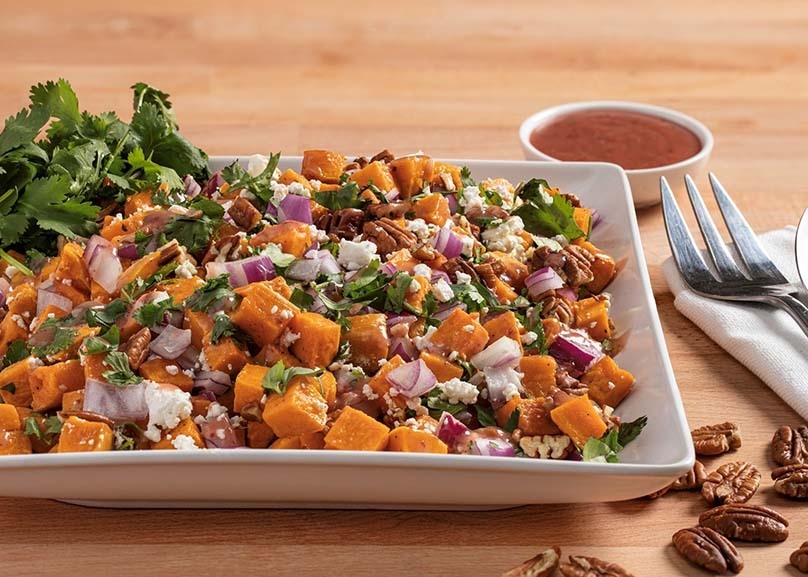 Roasted Sweet Potato Salad on plate with cranberry dressing, fork, napkin, pecans, wood table