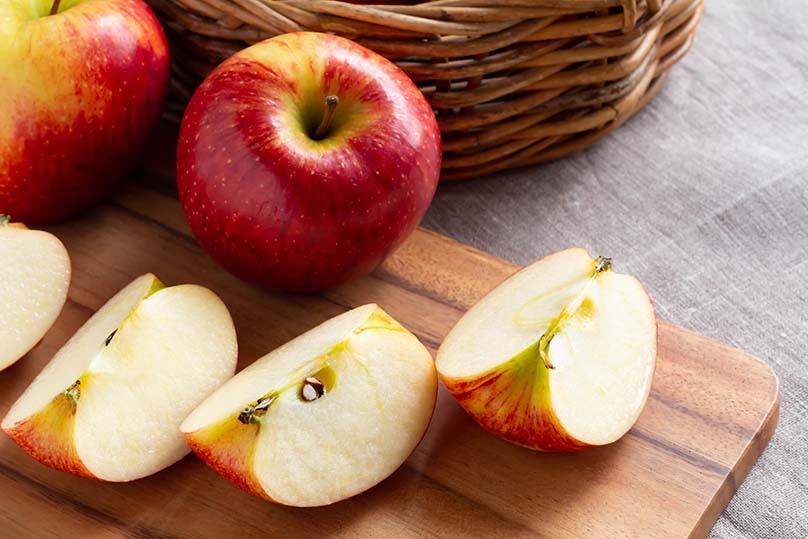 Apples, apple slices, wicker basket, wood cutting board, tablecloth