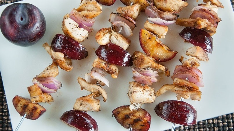 Grilled Chicken pieces and plum slices on skewers, fresh red plum, white cutting board