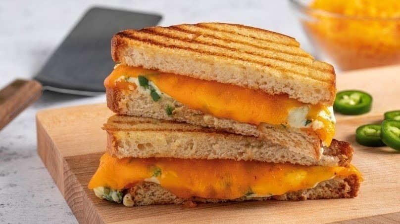 Jalapeno Popper Grilled Cheese sliced on cutting board, spatula, sliced jalapenos, cheese