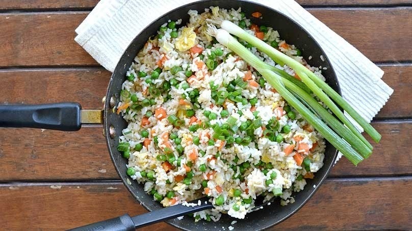 Vegetable fried rice with carrots, peas, green onions, eggs, and fried rice in pan, stirring spatula mixing ingredients