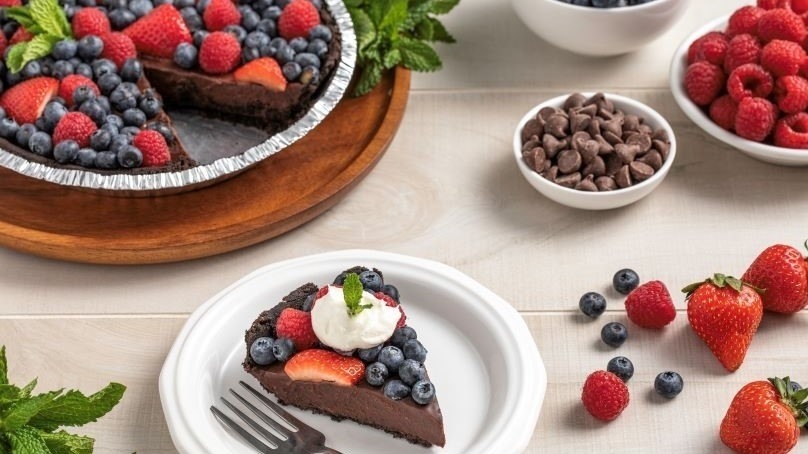 No bake chocolate berry pie, slice of pie on white paper plate, strawberries, blueberries on table, bowl of raspberries, bowl of chocolate chips