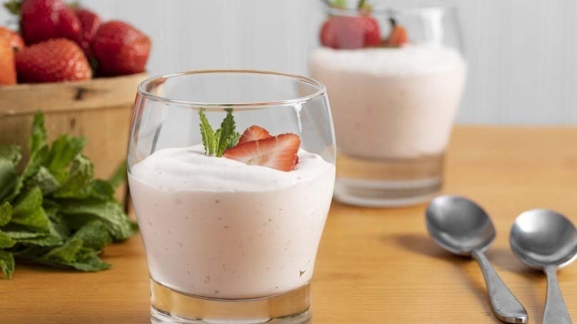 Strawberry Mousse in glass with sliced strawberry garnish, basket of strawberries, mint, spoons, wood table