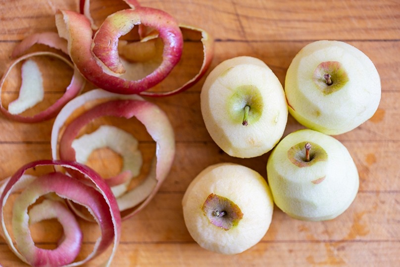 Four Fresh peeled apples on right, apple peels on left