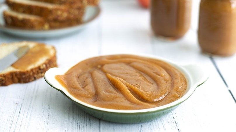 Serving dish of Apple butter, white wood table, sliced bread on plate in background