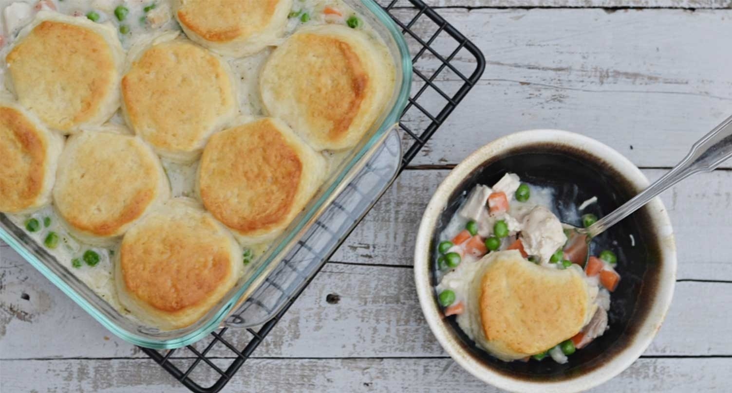 Chicken and Biscuit pot pie in bowl next to serving dish of chicken pot pie, wood table background