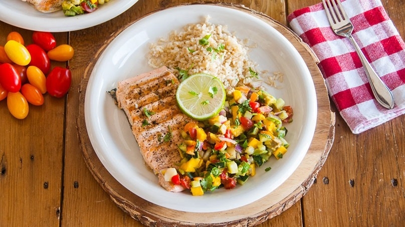 Cooked fish, rice and vegetables, fork, napkin, wood table