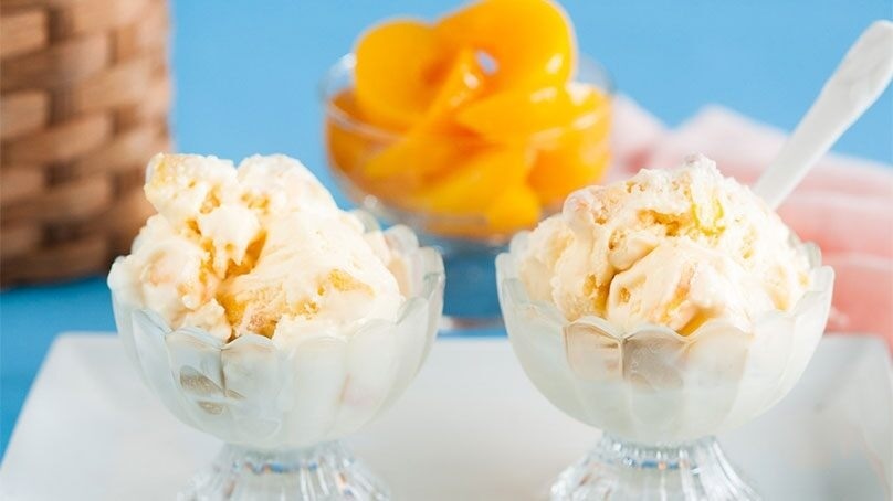 Two Homemade peach ice cream sundaes, peaches in serving bowl in background, blue wall in background