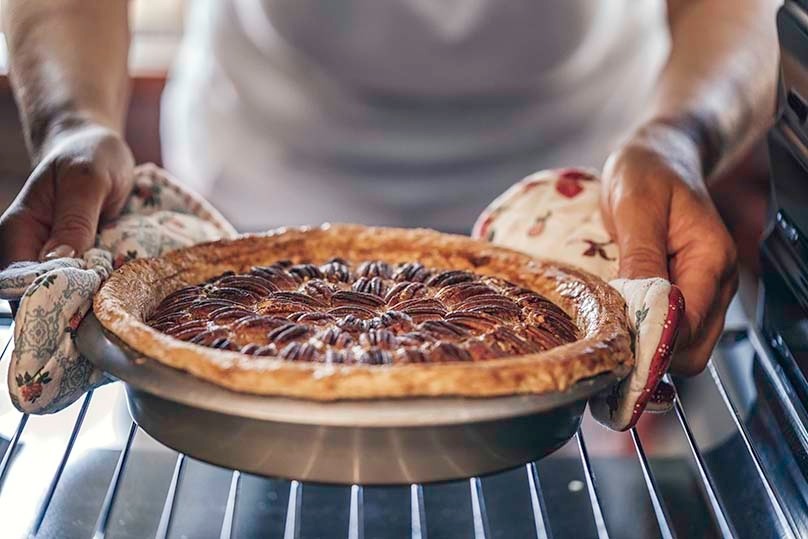 Woman Taking a Pecan Pie Out of the Oven for Thanksgiving Feast
