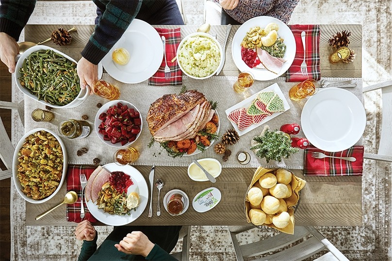 Top down view of dining table full with holiday dishes, people reaching for dishes to serve