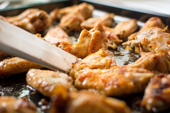 Cooking tongs holding barbecue chicken wings on black plate