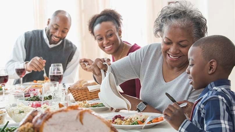 Famil having Thankshgiving dinner, grandmother pours gravy for grandson