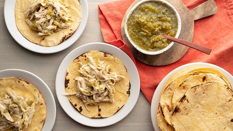 Salsa Verde Chicken Tacos on plates, dish of salsa verde, tortillas