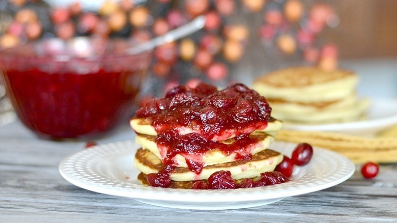 Cranberry sauce on a stack off pancakes, white plate, gray countertop, pancakes, bowl of sauce