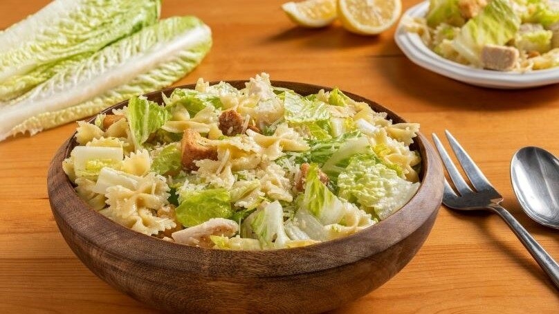 Chicken Caesar Pasta Salad n wodden bowl, wood table,, fork and spoon, 