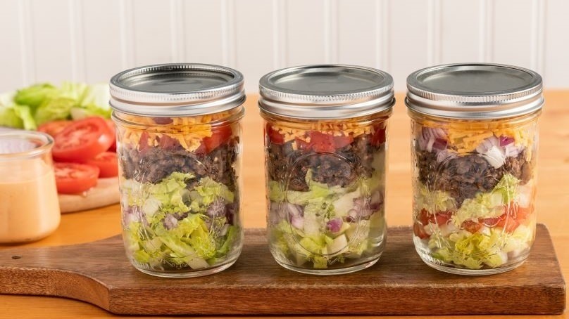 Low-Carb Cheeseburger Salad Mason Jars on cutting board, wood counter, small dish of dresing, tomates and lettuce on cutting board