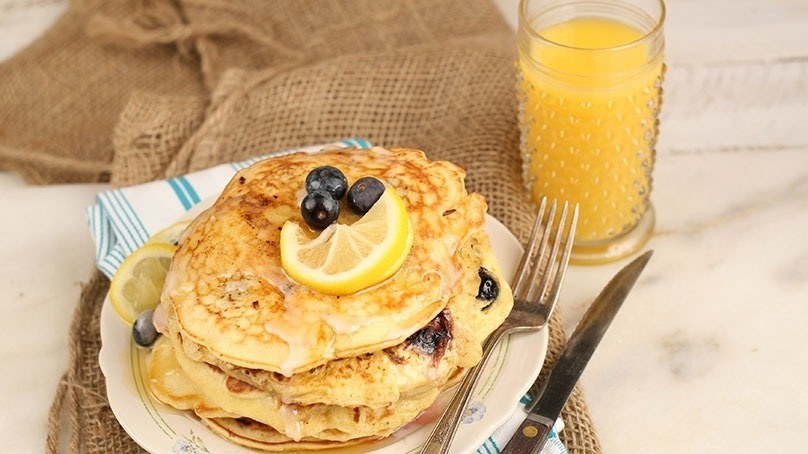  Lemon Blueberry Pancakes  on a plate with knife, fork and napkin, glass of orange juice