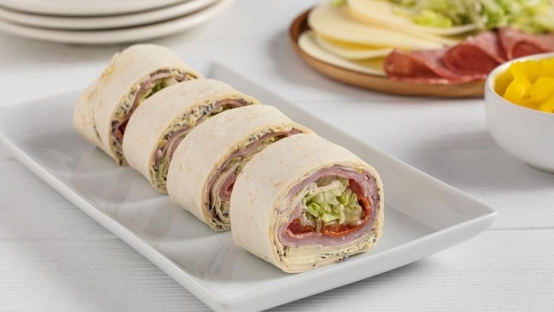  Cooler-Friendly Italian Sub Pinwheels on whit serving dish next to plate of ingredients