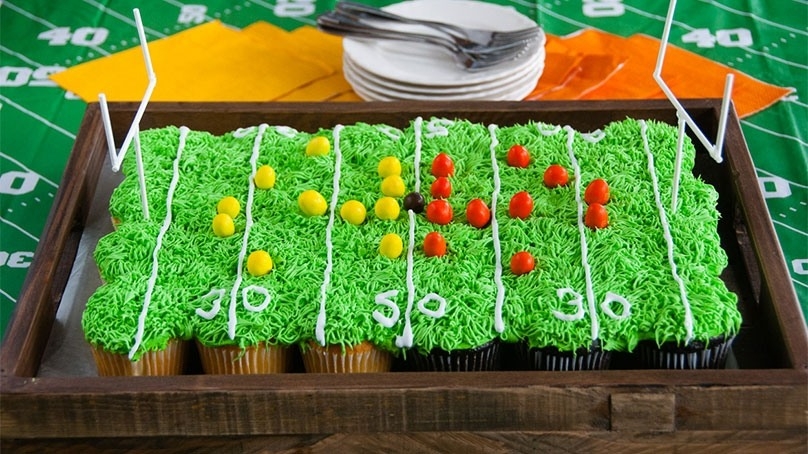 Cupcakes made to look like football field, peanut candies representing football players, dessert plates and forks, colorful napkins, football field table cloth