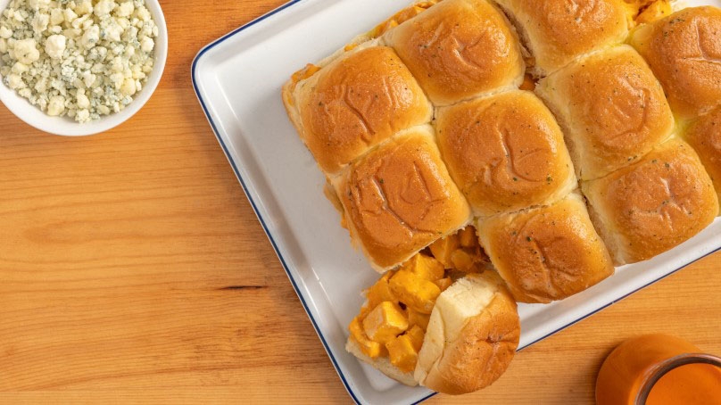 Baked Buffalo Chicken Sliders, lined baking sheet, blue cheese crumbles, buffalo sauce, wood table